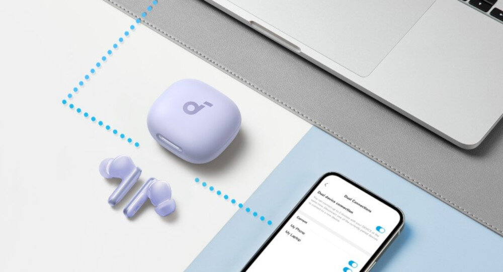 Na obrazie widoczne są fioletowe słuchawki dokanałowe z etui ładującym obok laptopa i smartfona. Na ekranie smartfona wyświetlone są ustawienia połączeń Bluetooth.