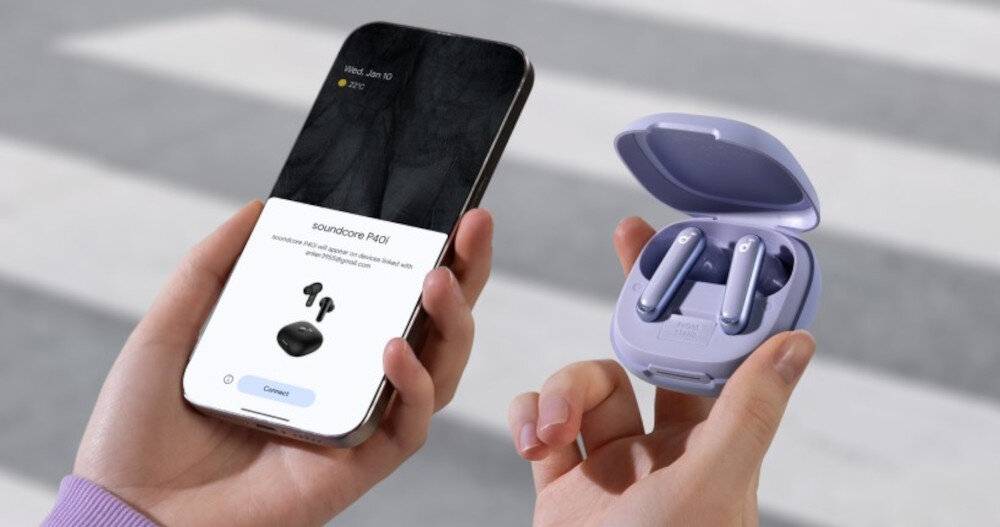Osoba trzyma w jednej ręce smartfon z wyświetlonym obrazem słuchawek dokanałowych SOUNDCORE P40i ANC, a w drugiej otwarte etui z fioletowymi słuchawkami. W tle widoczna jest rozmyta zebra na przejściu dla pieszych.