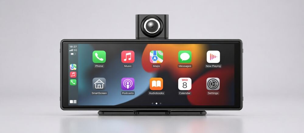 Na obrazie widoczny jest samochodowy tablet z dużym ekranem, na którym wyświetlane są ikony aplikacji takich jak Phone, Music, Maps, Messages, Now Playing, SmartScreen, Podcasts, Audiobooks, Calendar i Settings. Nad ekranem znajduje się kamera, a w rogu ekranu widoczny jest czas 18:27 i poziom sygnału sieci 5G.