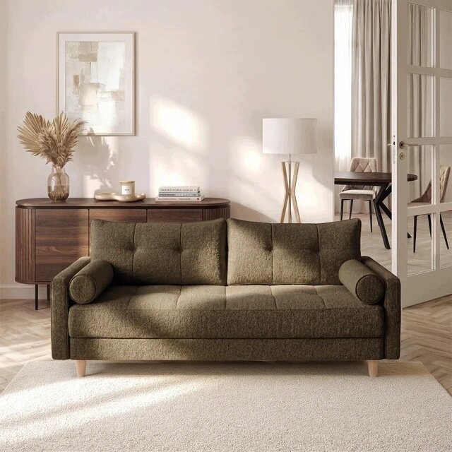 Brązowa sofa rozkładana z funkcją spania stoi na jasnym dywanie w eleganckim salonie. W tle znajduje się drewniana komoda z dekoracjami oraz lampa stojąca.