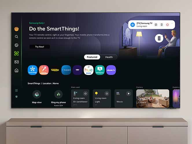 Telewizor wyświetla interfejs SmartThings z różnymi aplikacjami i opcjami sterowania. Na ekranie widoczny jest tekst: \'Do the SmartThings! Your TV remote control, right at your fingertips. Your mobile phone transforms into a remote control as soon as it is close enough to the TV.\'