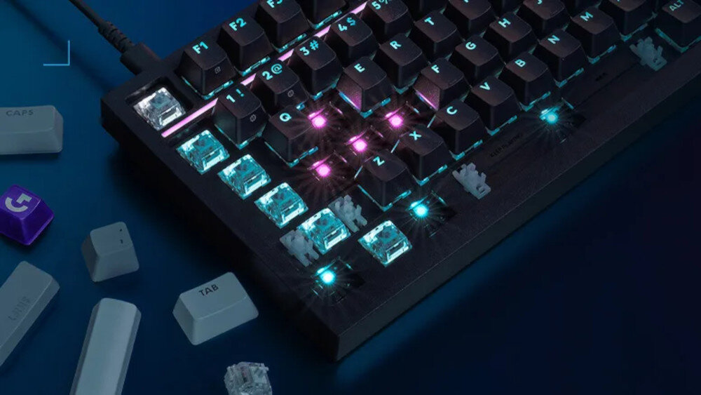 Klawiatura mechaniczna z podświetleniem RGB, z widocznymi klawiszami F1-F12 oraz literami Q, W, E, R, A, S, D, Z, X, C. Obok klawiatury znajdują się luźne klawisze i przełączniki, w tym klawisze z napisem \'CAPS\' i \'TAB\'.