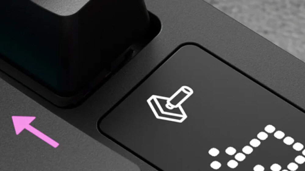 Zbliżenie na klawisz klawiatury z białym symbolem joysticka na czarnym tle oraz różową strzałką obok.
