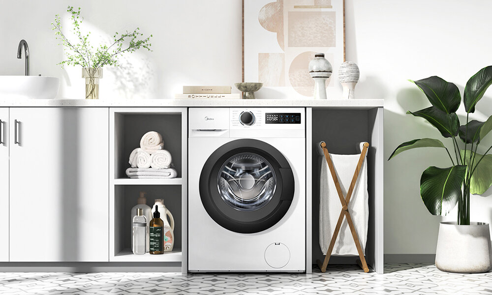 PRALKA MIDEA MF110W90BA10/WB-PL Pralka Midea zabudowana pod blatem w jasnej pralni lub łazience. Grafika prezentuje urządzenie w otoczeniu półek na ręczniki i środki do prania