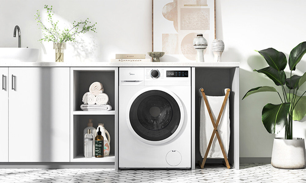 PRALKA MIDEA MF110W90BA10/WW-PL Pralka Midea zabudowana pod blatem w jasnej pralni lub łazience. Grafika prezentuje urządzenie w otoczeniu półek na ręczniki i środki do prania