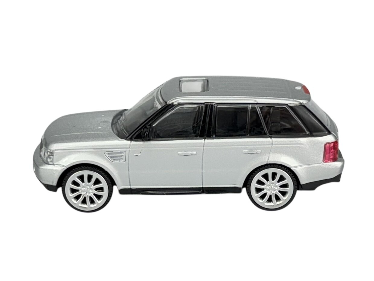 Model samochodu w skali 1:43, przedstawiający srebrny SUV z czarnymi szybami i białymi felgami. Pojazd ma szczegółowo odwzorowane elementy, takie jak lusterka boczne i klamki.