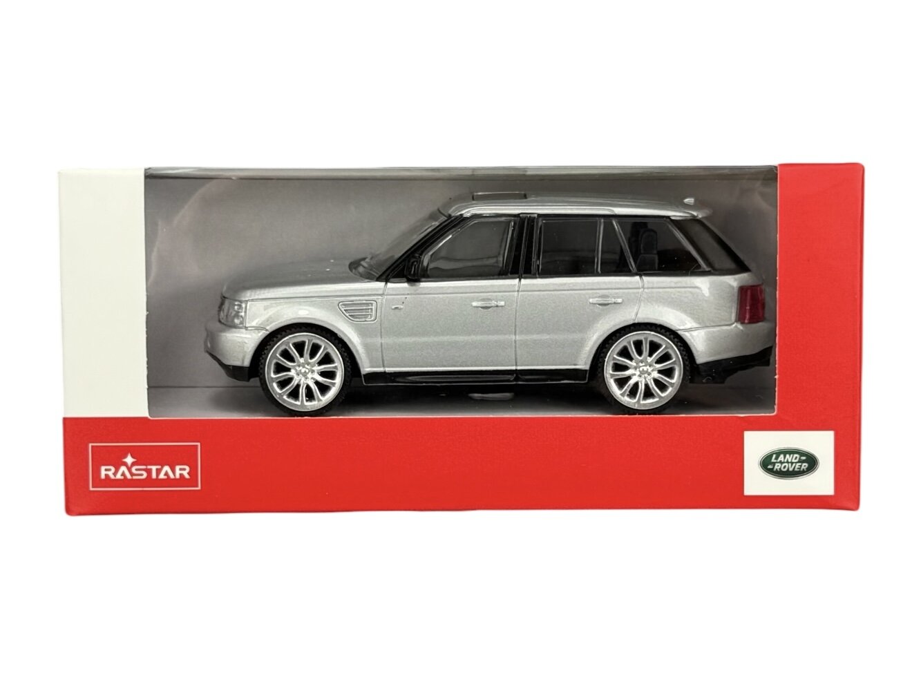 Model samochodu w skali 1:43 w kolorze srebrnym, umieszczony w czerwonym opakowaniu z logo \'RASTAR\' i \'LAND ROVER\'.