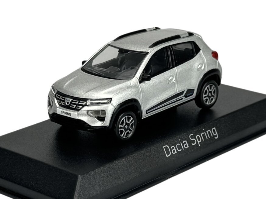 Model samochodu w kolorze srebrnym umieszczony na czarnej podstawce z napisem \'Dacia Spring\'.
