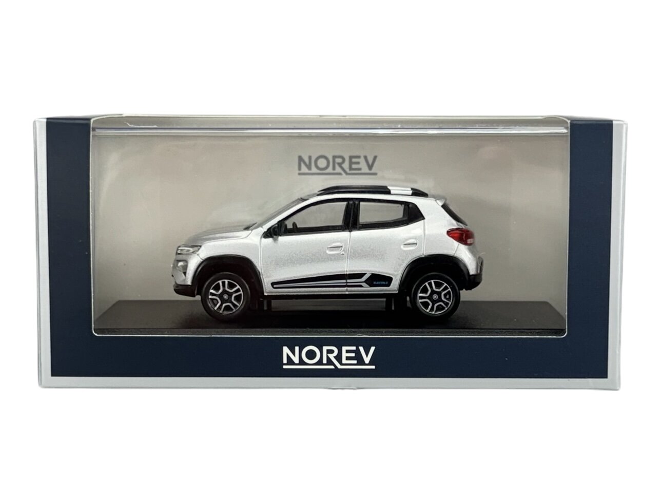 Model samochodu w skali 1:43 w srebrnym kolorze, umieszczony w przezroczystym opakowaniu z napisem \'NOREV\'.