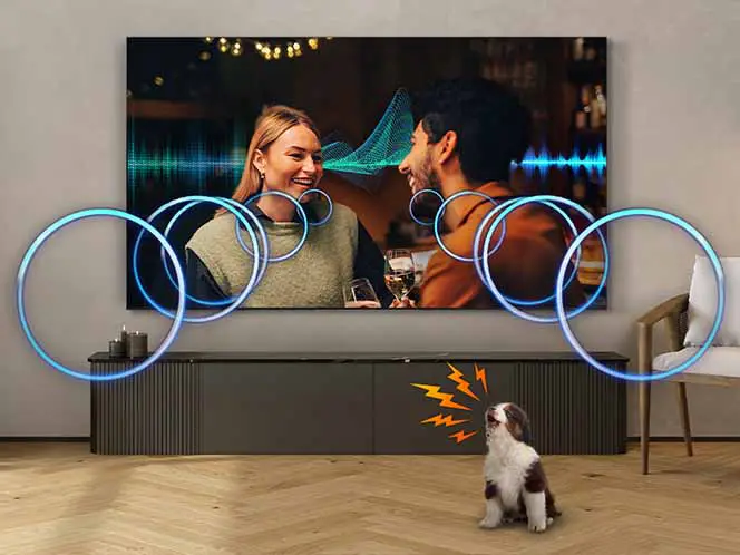 Na ścianie wisi duży telewizor, na którym widać dwie osoby rozmawiające w barze. Przed telewizorem stoi pies, a wokół niego i na ekranie widoczne są kolorowe kręgi i fale dźwiękowe.