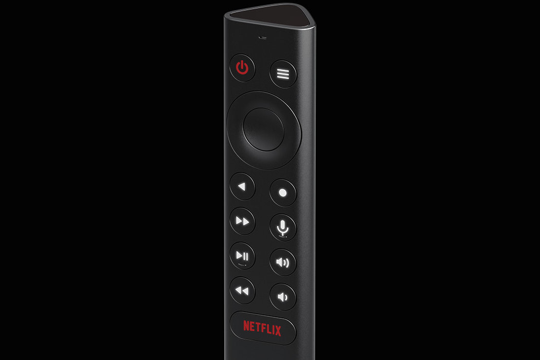 Czarny pilot z przyciskami, w tym przycisk z logo \'Netflix\' na dole. Widoczne są także przyciski z symbolami zasilania, menu, nawigacji, mikrofonu i regulacji głośności.