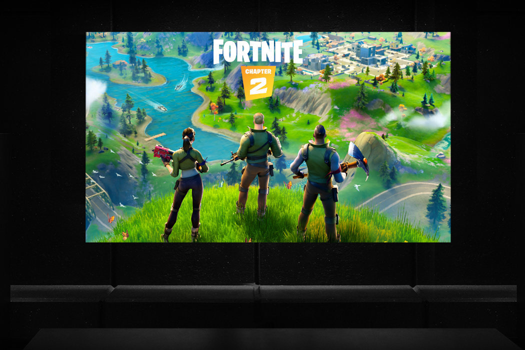 Obraz przedstawia trzech postaci stojących na wzgórzu z widokiem na kolorowy krajobraz z rzeką i budynkami. Na górze widnieje napis \'FORTNITE CHAPTER 2\'.