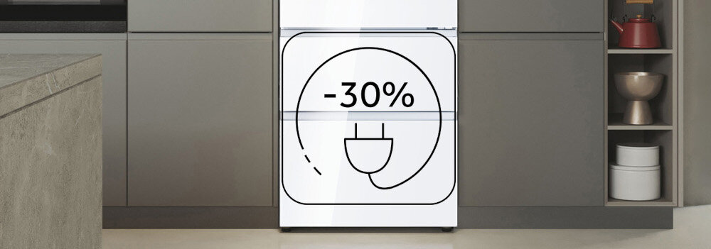 Biała lodówka z symbolem wtyczki i napisem \'-30%\' na drzwiach, ustawiona w nowoczesnej kuchni z szarymi szafkami.