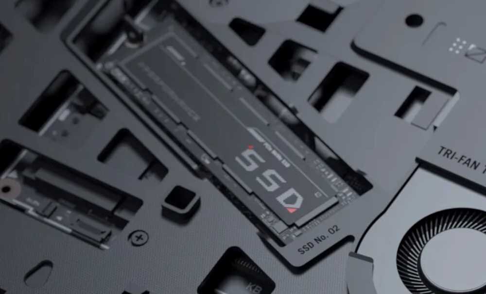 Zbliżenie na wnętrze laptopa z widocznym dyskiem SSD oznaczonym jako \'SSD No. 02\'. Obok znajduje się wentylator z napisem \'TRI-FAN\'.