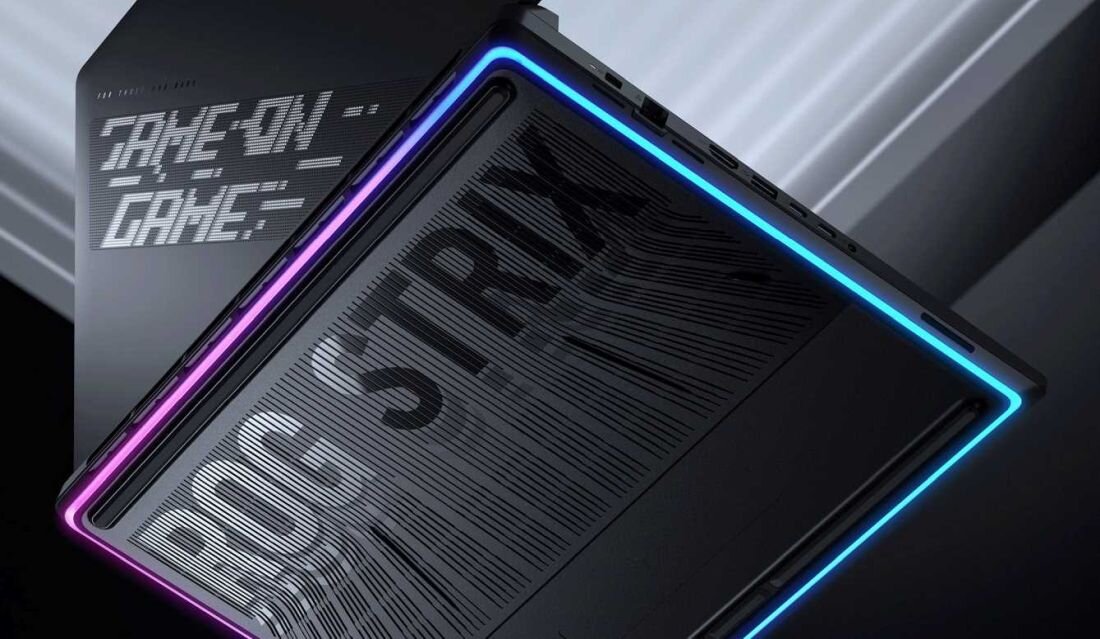 Obraz przedstawia laptop z podświetleniem LED w kolorach fioletowym i niebieskim. Na obudowie widoczny jest napis \'GAME ON GAME\' oraz \'ROG STRIX\'.