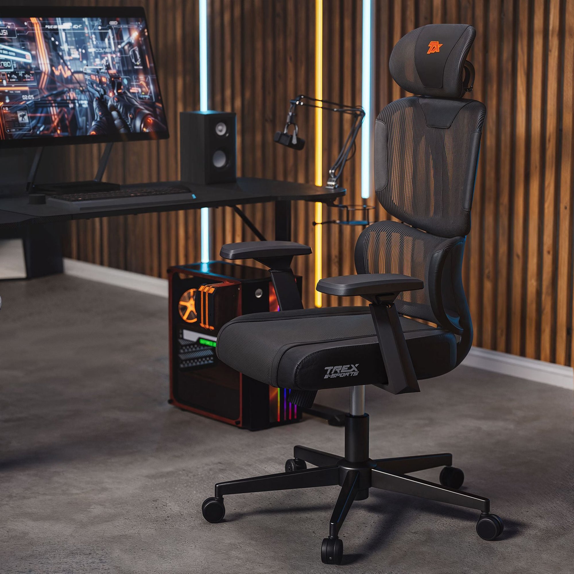 Na obrazie znajduje się czarny fotel gamingowy z siatkowanym oparciem i podłokietnikami, na którym widnieje napis \'TREX E-SPORTS\'. W tle widać biurko z monitorem, głośnikiem i komputerem z podświetleniem RGB.