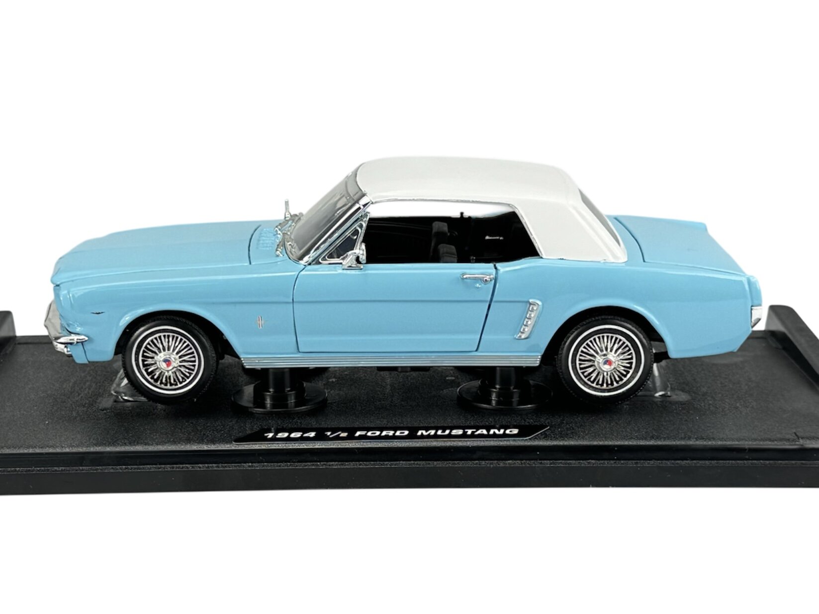 Model samochodu w kolorze niebieskim z białym dachem, umieszczony na czarnej podstawce z napisem \'1964 1/2 Ford Mustang\'.