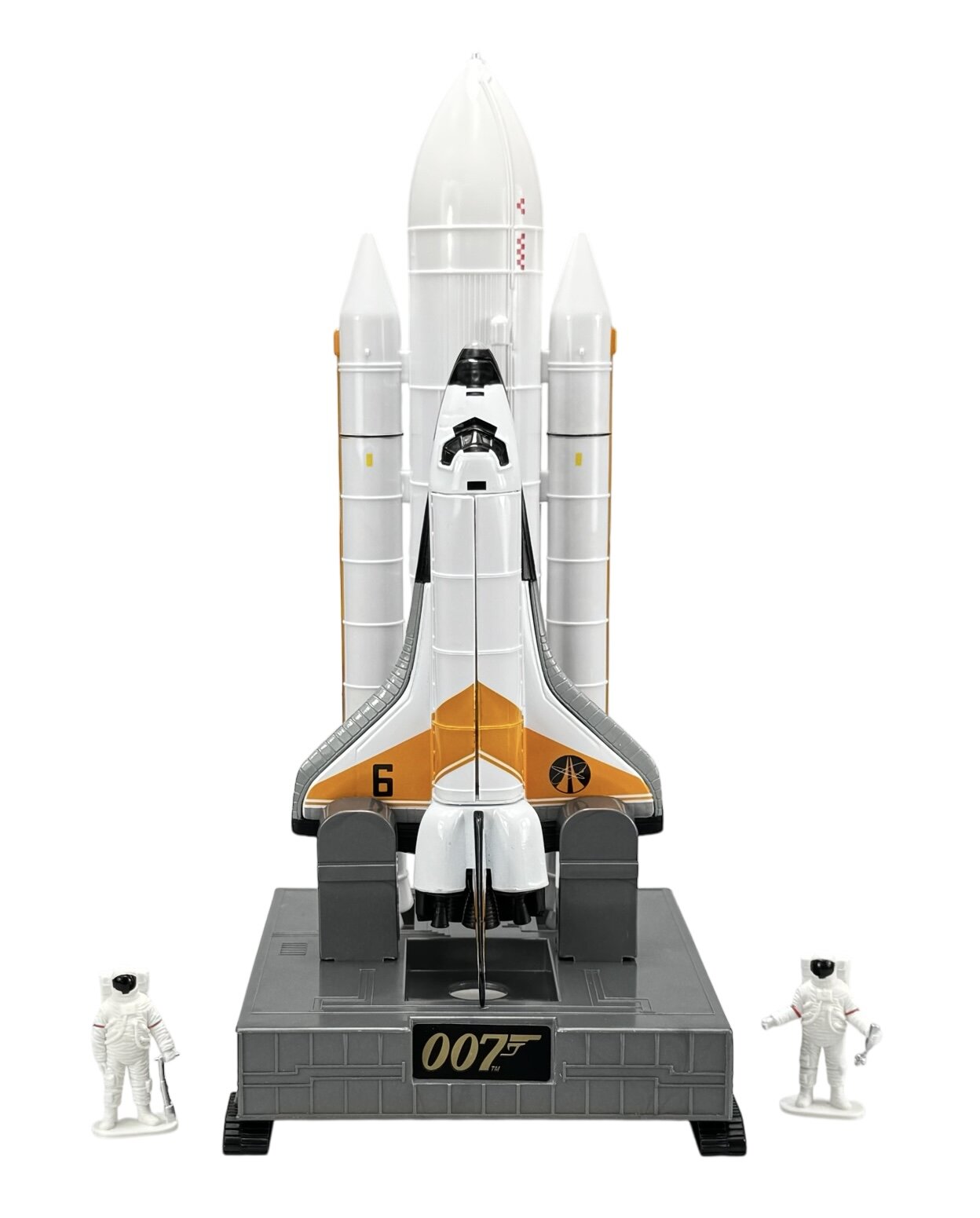 Model wahadłowca kosmicznego z napisem \'007\' na podstawie, otoczony dwoma figurkami astronautów. Wahadłowiec jest biały z pomarańczowymi i czarnymi elementami oraz oznaczeniem \'6\'.