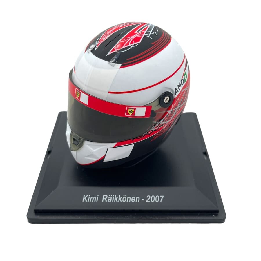 Model kasku wyścigowego w kolorach czerwonym, białym i czarnym, umieszczony na podstawce z napisem \'Kimi Räikkönen - 2007\'. Na kasku widoczne są logotypy Ferrari i AMD.