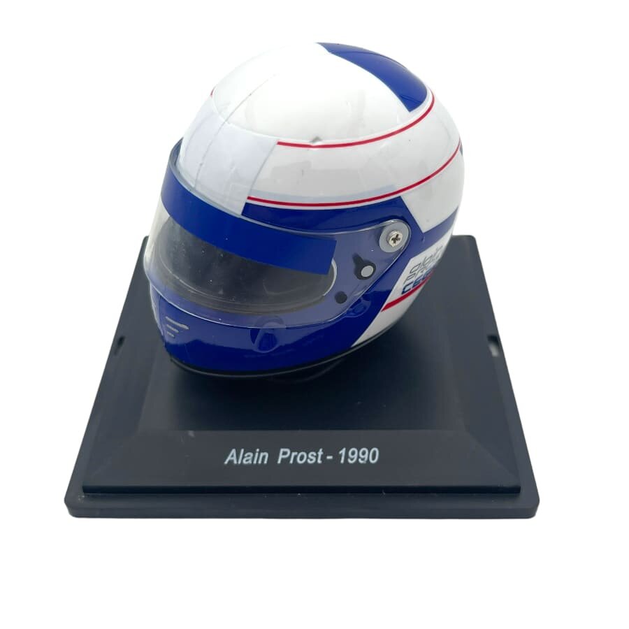 Model kasku w kolorach białym, niebieskim i czerwonym, umieszczony na czarnej podstawce z napisem \'Alain Prost - 1990\'.