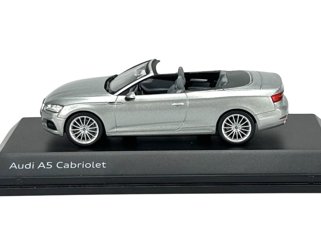 Model samochodu Audi A5 Cabriolet w kolorze srebrnym, umieszczony na czarnej podstawce z napisem \'Audi A5 Cabriolet\'.