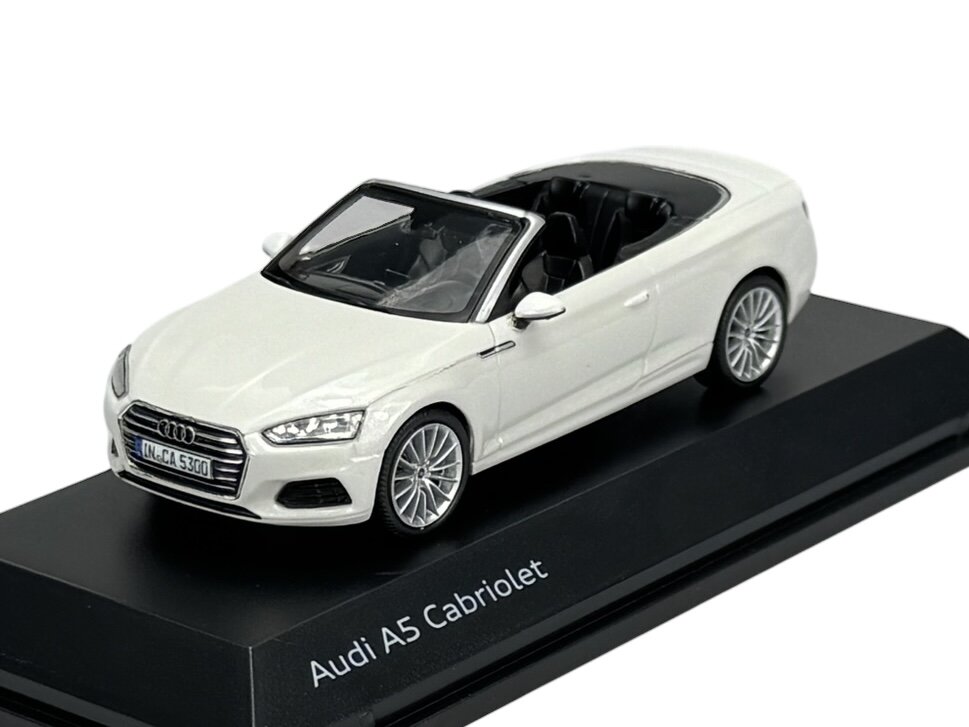 Model samochodu Audi A5 Cabriolet w kolorze białym, umieszczony na czarnej podstawce z napisem \'Audi A5 Cabriolet\'.