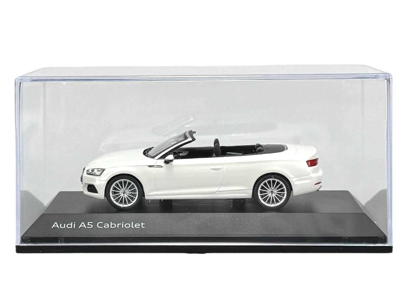 Model samochodu Audi A5 Cabriolet w kolorze białym, umieszczony w przezroczystej gablocie. Na podstawce widoczny jest napis \'Audi A5 Cabriolet\'.