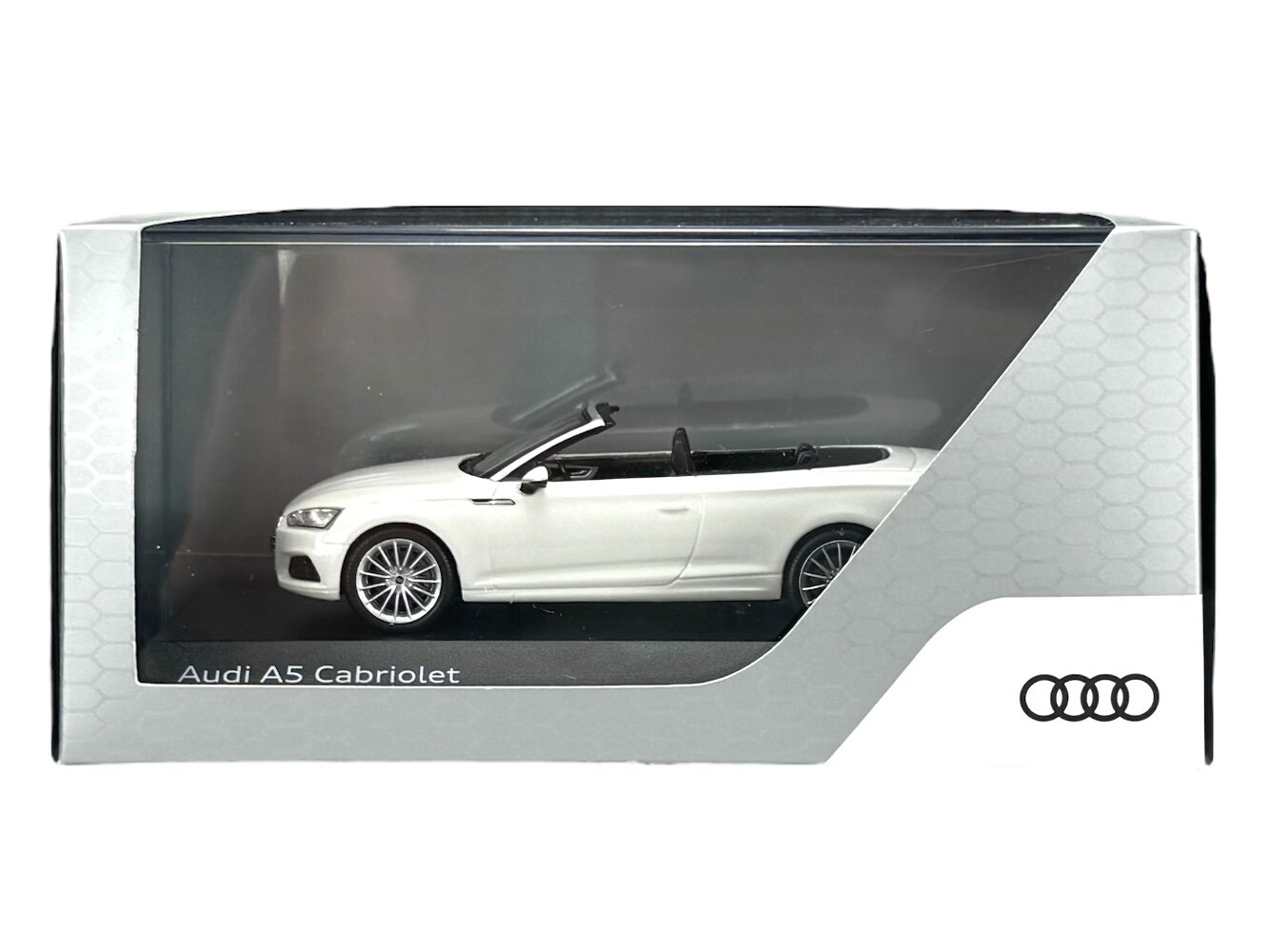 Model samochodu Audi A5 Cabriolet w kolorze białym znajduje się w przezroczystym opakowaniu z napisem \'Audi A5 Cabriolet\'. Widoczne jest logo Audi z czterema pierścieniami.