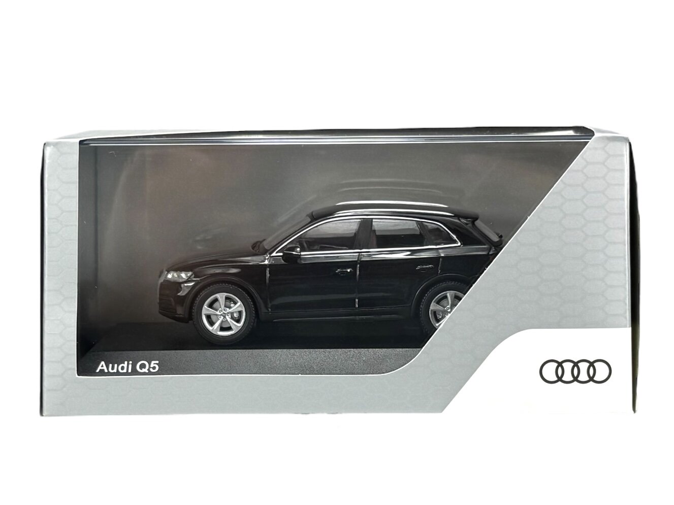 Model samochodu Audi Q5 w kolorze czarnym znajduje się w przezroczystym opakowaniu z napisem \'Audi Q5\'. Widoczne jest logo Audi z czterema pierścieniami.