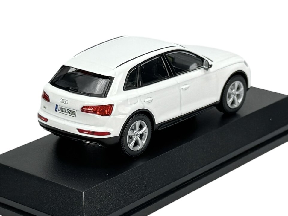 Model samochodu w kolorze białym na czarnej podstawce, z widocznym logo Audi i tablicą rejestracyjną \'IN Q5 20\'.