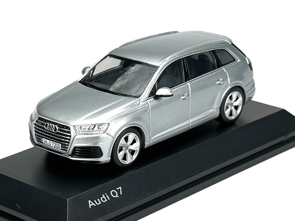 Model samochodu Audi Q7 w kolorze srebrnym, umieszczony na czarnej podstawce z napisem \'Audi Q7\'.