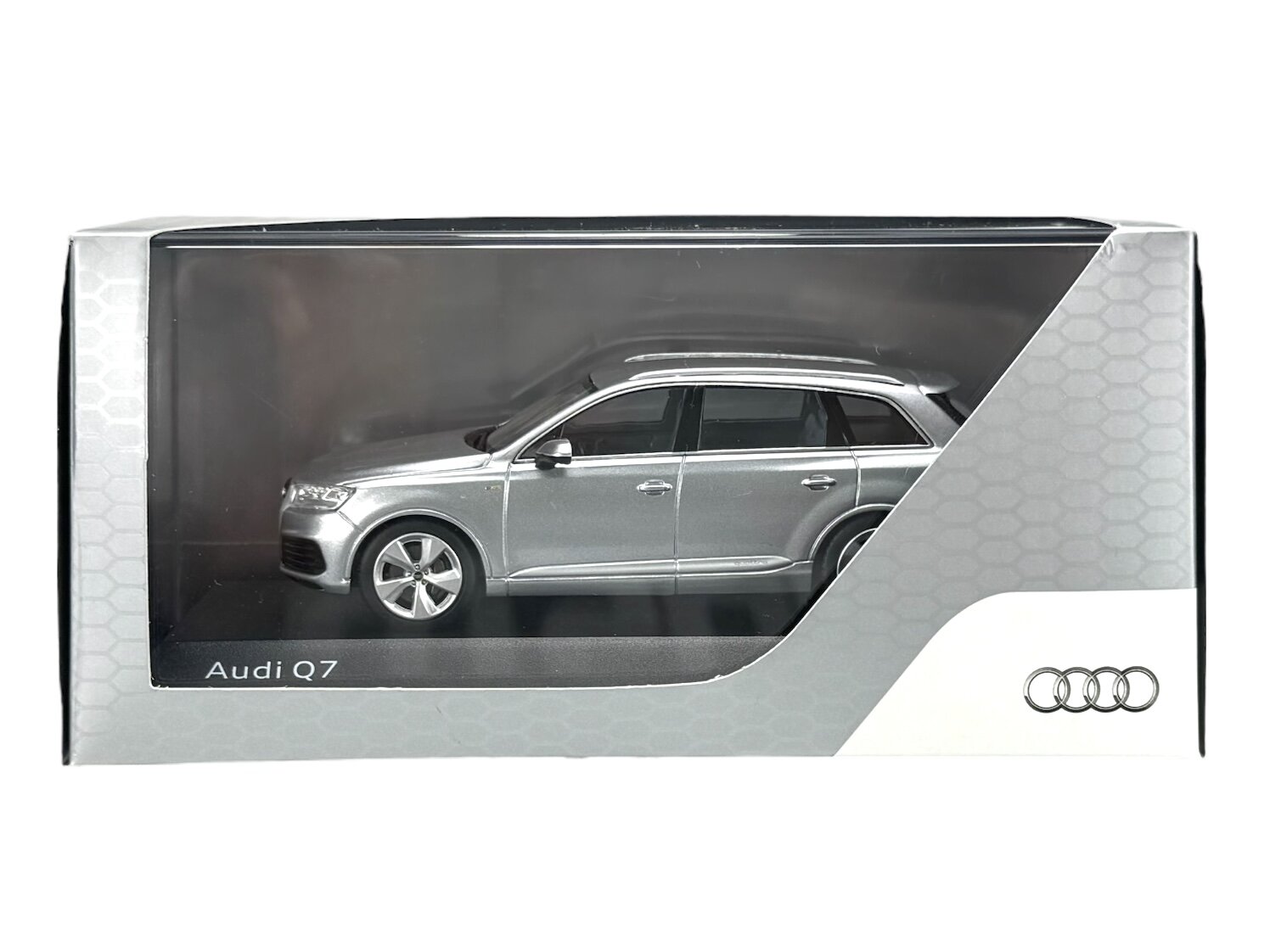 Model samochodu Audi Q7 w kolorze srebrnym znajduje się w przezroczystym opakowaniu z napisem \'Audi Q7\'. Na opakowaniu widoczne jest logo Audi.