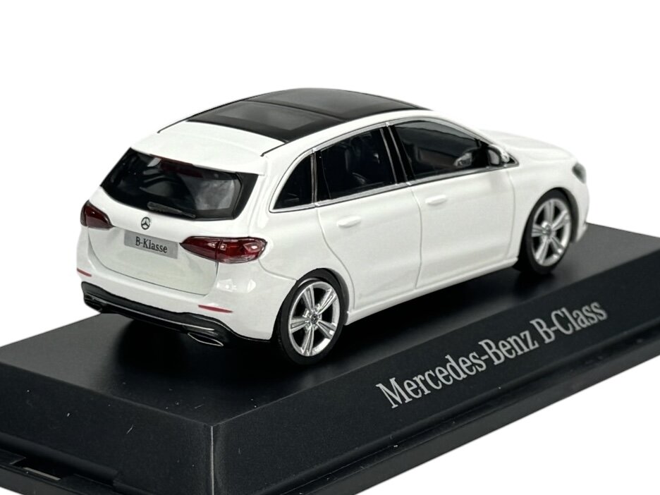 Model samochodu w kolorze białym z czarnym dachem, umieszczony na podstawce z napisem \'Mercedes-Benz B-Class\'. Na tylnej tablicy rejestracyjnej widnieje napis \'B-Klasse\'.