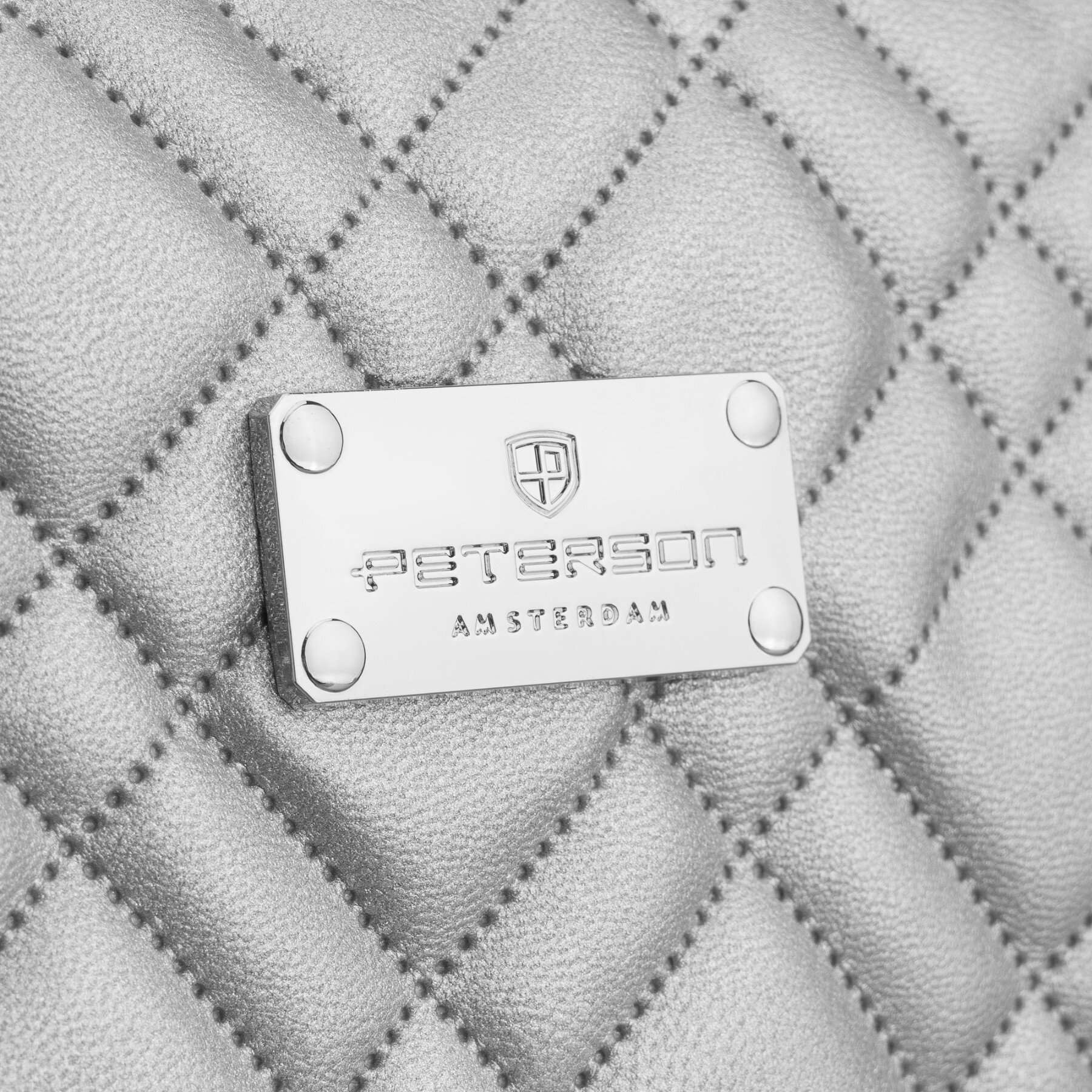 Srebrna, pikowana powierzchnia z metalową tabliczką z napisem \'PETERSON AMSTERDAM\'.