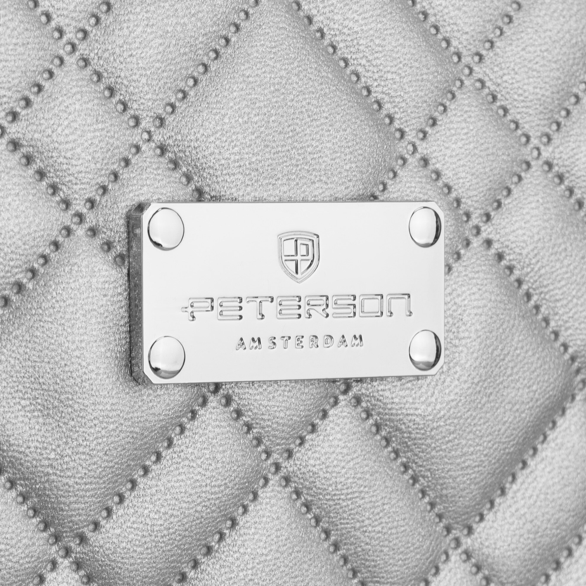 Srebrna, pikowana powierzchnia z metalową tabliczką z napisem \'PETERSON AMSTERDAM\' oraz logo w kształcie tarczy.