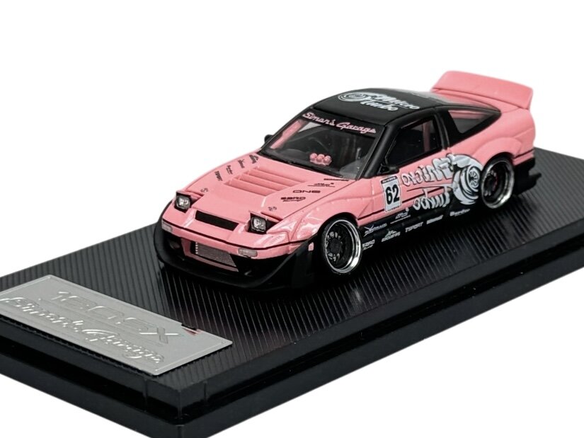 Model samochodu w skali 1:64 w kolorze różowym z czarnymi i białymi detalami, umieszczony na czarnej podstawce z napisem \'Tarmac Works\'.