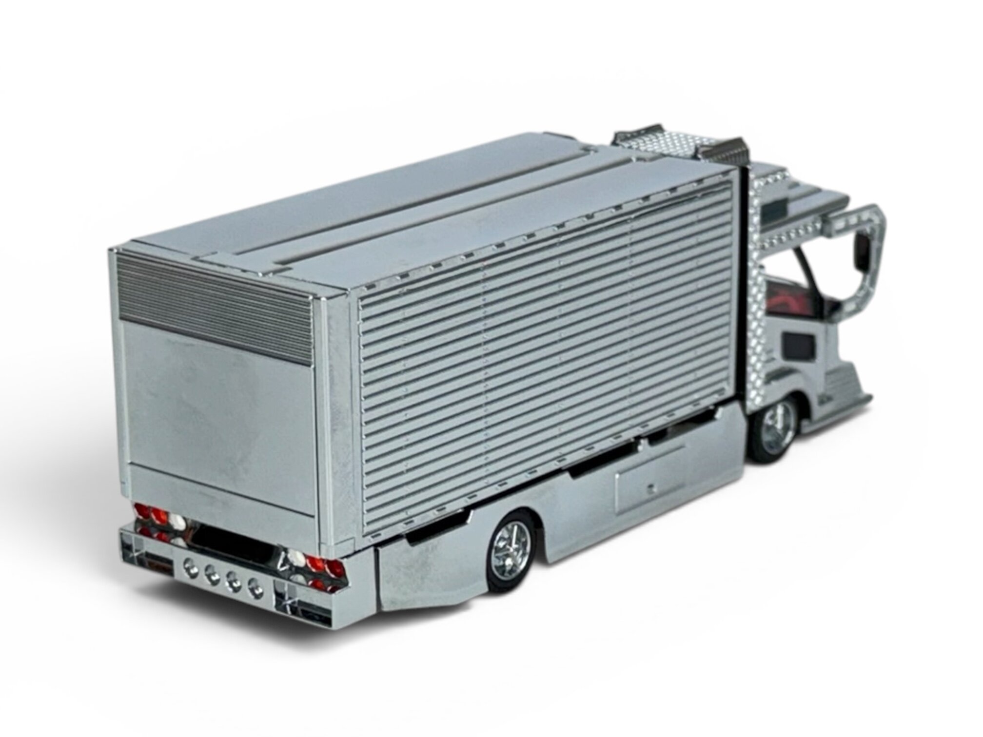 Model metalowej ciężarówki z kontenerem w skali 1:64, w kolorze srebrnym, z widocznymi detalami takimi jak reflektory i koła.