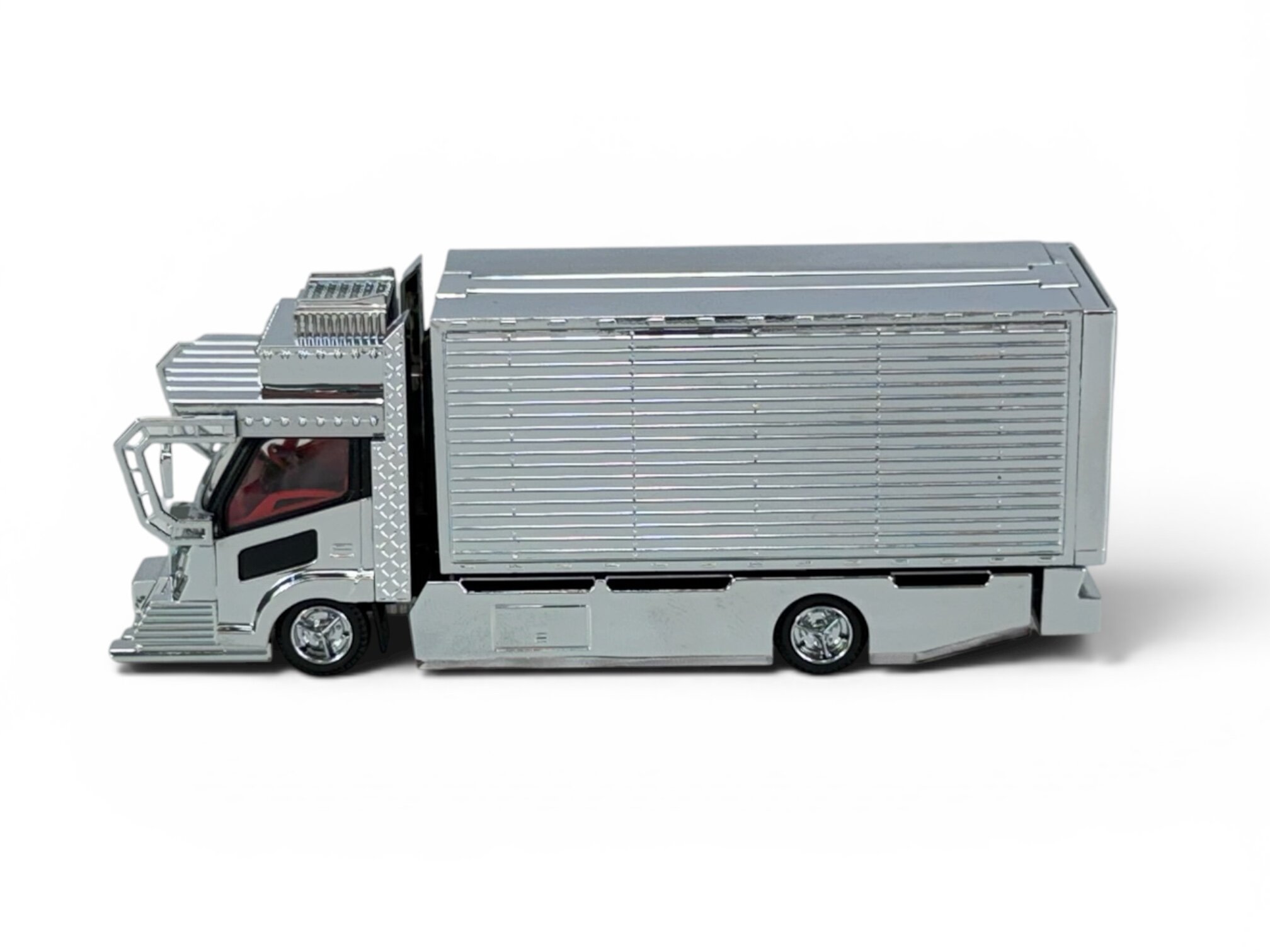 Model ciężarówki w skali 1:64 z metalowym kontenerem, w kolorze srebrnym, z widocznymi detalami kabiny i kół.