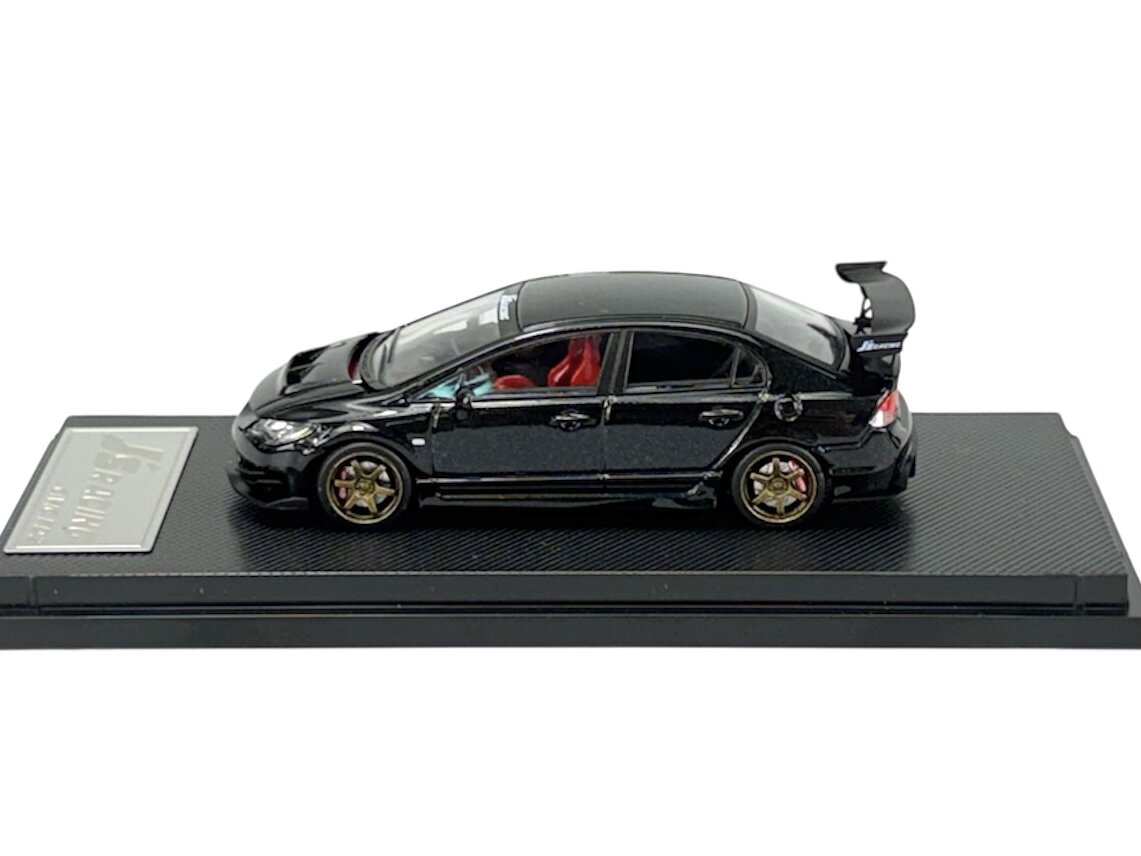 Model samochodu w skali 1:64 przedstawiający czarny pojazd sportowy z czerwonym wnętrzem, umieszczony na podstawce. Na podstawce widoczne jest logo \'J\'s Racing\'.