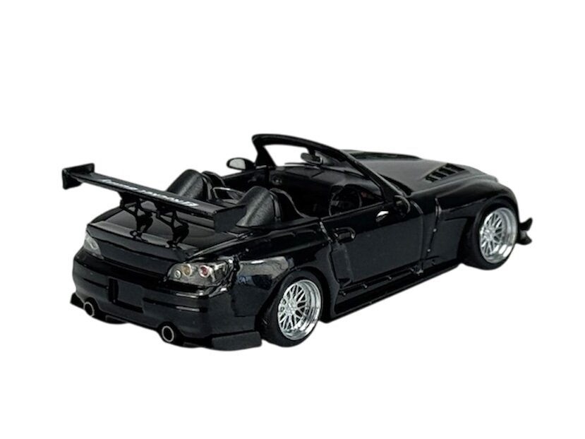 Czarny model samochodu sportowego w skali 1:64 z widocznym dużym tylnym spojlerem i szczegółowymi felgami. Samochód ma otwarty dach i dwa miejsca siedzące.