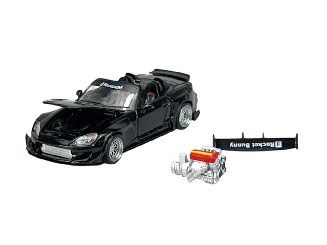 Czarny model samochodu sportowego w skali 1:64 z otwartym dachem, obok którego znajdują się dodatkowe elementy, takie jak spojler z napisem \'Rocket Bunny\' i miniaturowy silnik. Na przedniej szybie widoczny jest napis \'Pandem\'.