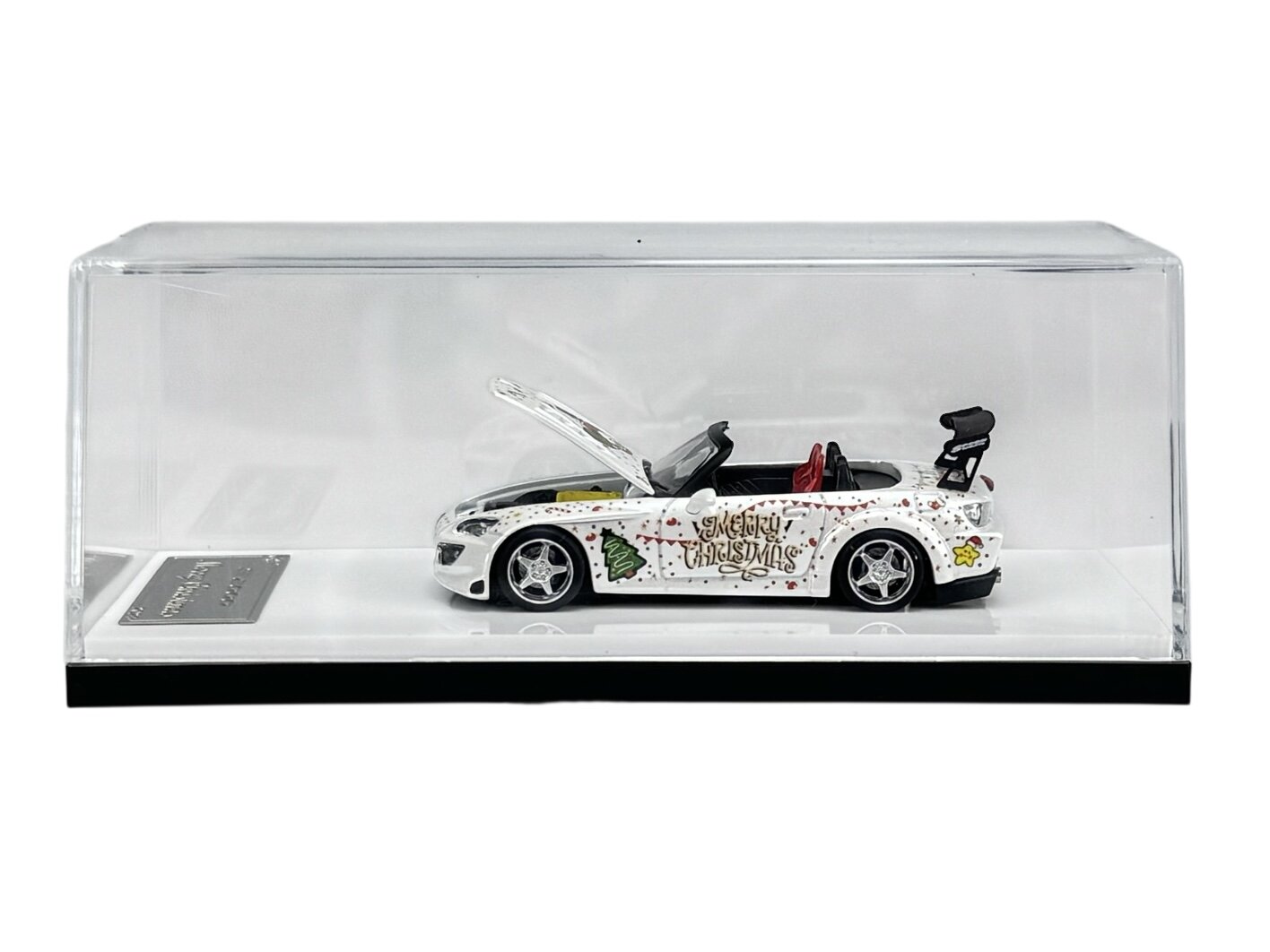 Model samochodu w skali 1:64 w przezroczystej gablocie, ozdobiony świątecznymi motywami i napisem \'Merry Christmas\'.