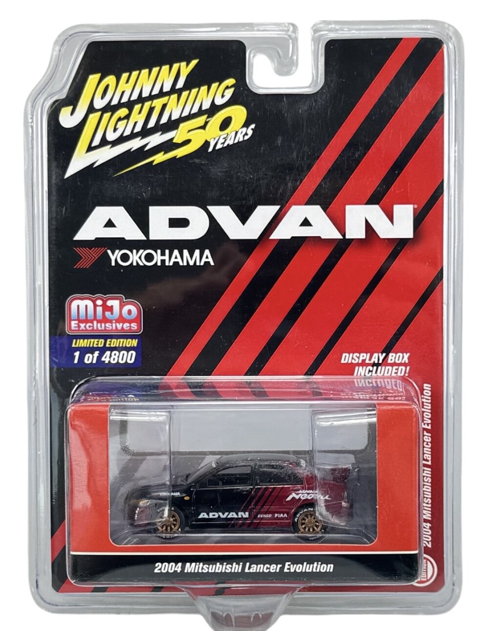 Opakowanie modelu samochodu z napisem \'Johnny Lightning 50 Years\', \'ADVAN\', \'YOKOHAMA\', \'miJo Exclusives\', \'LIMITED EDITION 1 of 4800\', \'DISPLAY BOX INCLUDED!\', \'2004 Mitsubishi Lancer Evolution\'. Wewnątrz znajduje się czarny model samochodu z czerwonymi i białymi napisami oraz złotymi felgami.