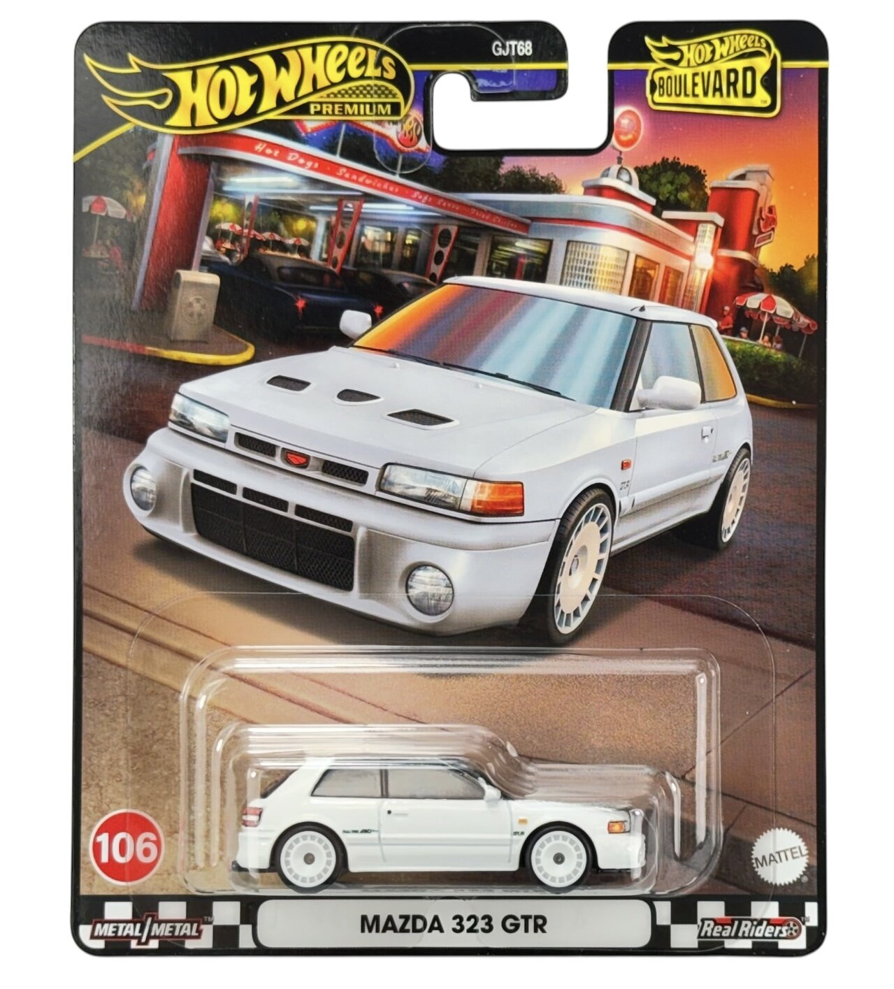 Opakowanie z modelem samochodu Hot Wheels Premium przedstawiające białą Mazdę 323 GTR na tle retro restauracji. Widoczne napisy to: \'Hot Wheels Premium\', \'Boulevard\', \'106\', \'Metal/Metal\', \'Real Riders\', \'MAZDA 323 GTR\'.