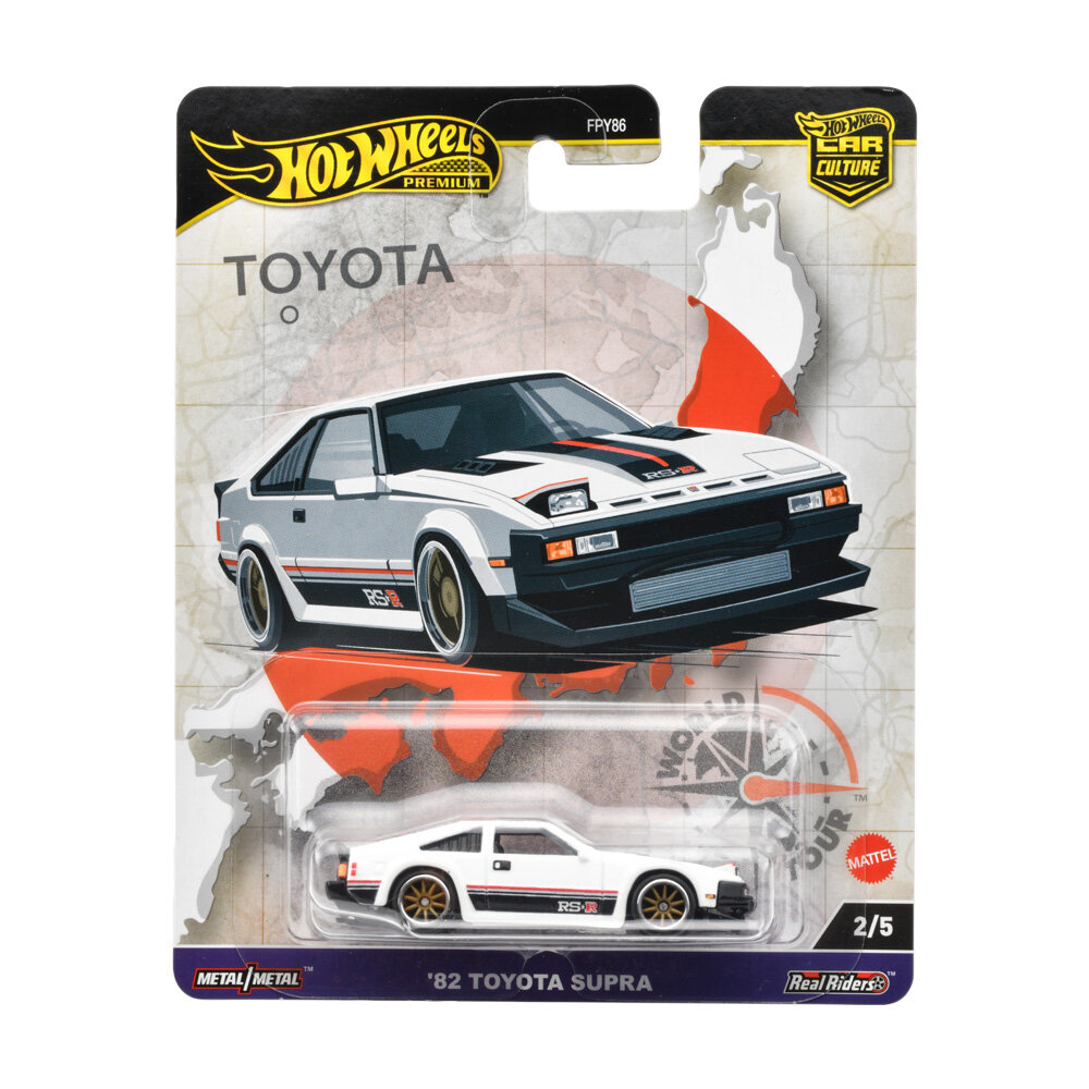 Opakowanie z modelem samochodu \'82 Toyota Supra w kolorze białym z czarnymi i czerwonymi detalami. Na opakowaniu widoczne są napisy: \'Hot Wheels Premium\', \'Toyota\', \'Metal/Metal\', \'Real Riders\', \'Mattel\', \'2/5\'.