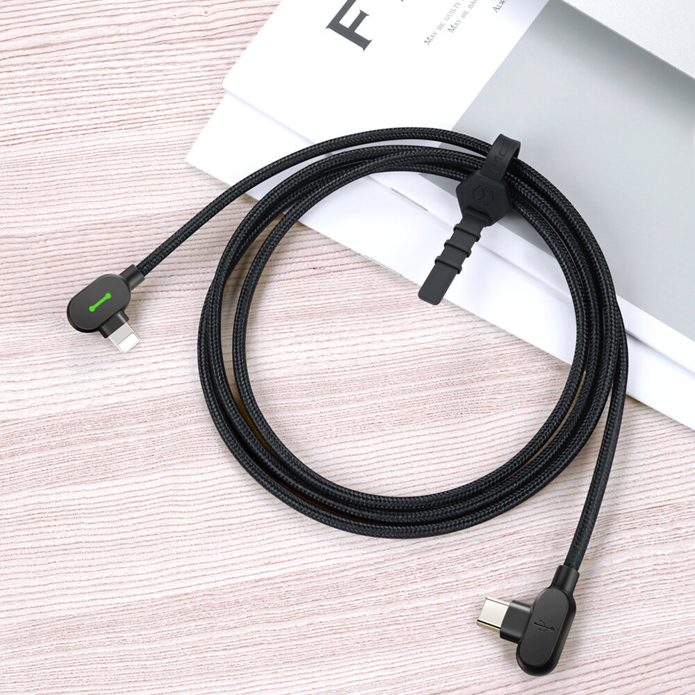 Czarny kabel z końcówkami USB-C i Lightning, z zielonym wskaźnikiem LED na jednej z wtyczek, leży na drewnianej powierzchni obok białej kartki papieru.
