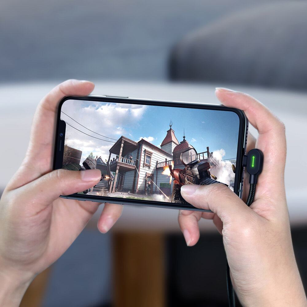 Osoba trzyma smartfon, na którym wyświetlana jest gra wideo z widokiem na budynek i postać z bronią. Do telefonu podłączony jest kabel z zielonym wskaźnikiem LED.