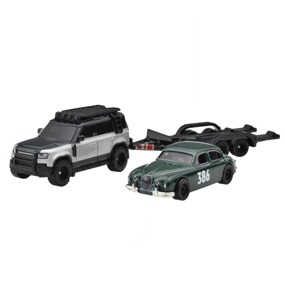 Na obrazie znajdują się dwa metalowe modele samochodów: srebrny SUV z napisem \'Defender\' na masce oraz zielony klasyczny samochód z numerem \'386\' na drzwiach. Obok nich widoczna jest czarna przyczepa.