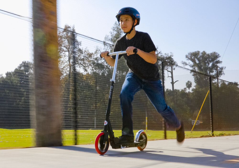 Hulajnoga RAZOR Carbon Lux 13073003 Czarny chłopak jedzie na hulajnodze po drodze niepowtarzalny design funkcjonalność niezapomnianą frajdę z jazdy ergonomiczna konstrukca solidne materiały dla dzieci w wieku od 8 lat czarna rozwój koordynacji ruchowej równowagi kondycji dziecka uniwersalny design dla dziewczynek i chłopców