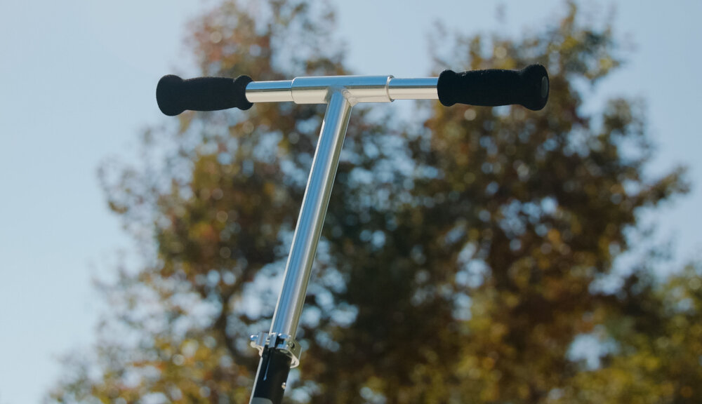 Hulajnoga RAZOR Carbon Lux 13073003 Czarny zbliżenie na kierownicę na tle nieba regulacja kierownicy w zakresie 84-101 cm dostosowanie do wzrostu użytkowanika piankowe rączki chronią dłonie przed otarciami pewny chwyt